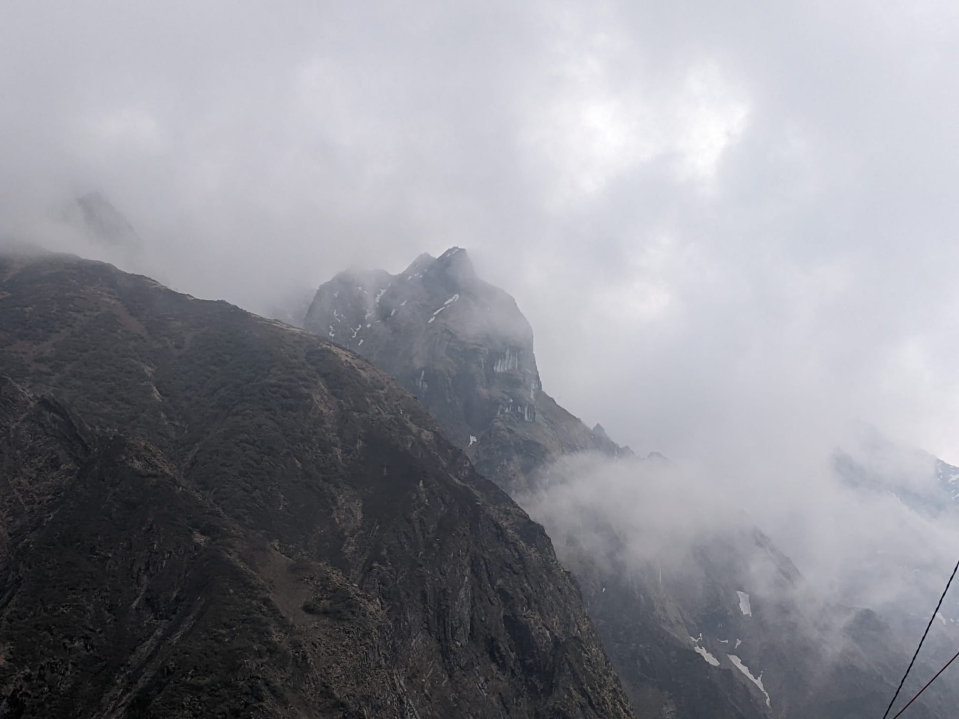 A high rock peak holding snow, seen through cloud from the region